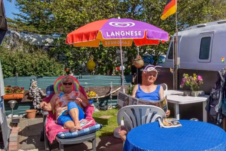 Camping Fluegger Strand Gaeste sonnen sich vor ihrem Wohnwagen 768x512
