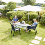 Ostsee Freizeitpark Booknis Gaeste vom Campingplatz sitzen unter dem Sonnenschirm auf dem Rasen 150x150